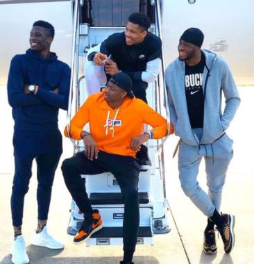 Four of Charles Antetokounmpo five sons, Alex in a blue hoodie, Kostas in an Orange, Thanasis in a grey, and Giannis Antetokounmpo in black and white.